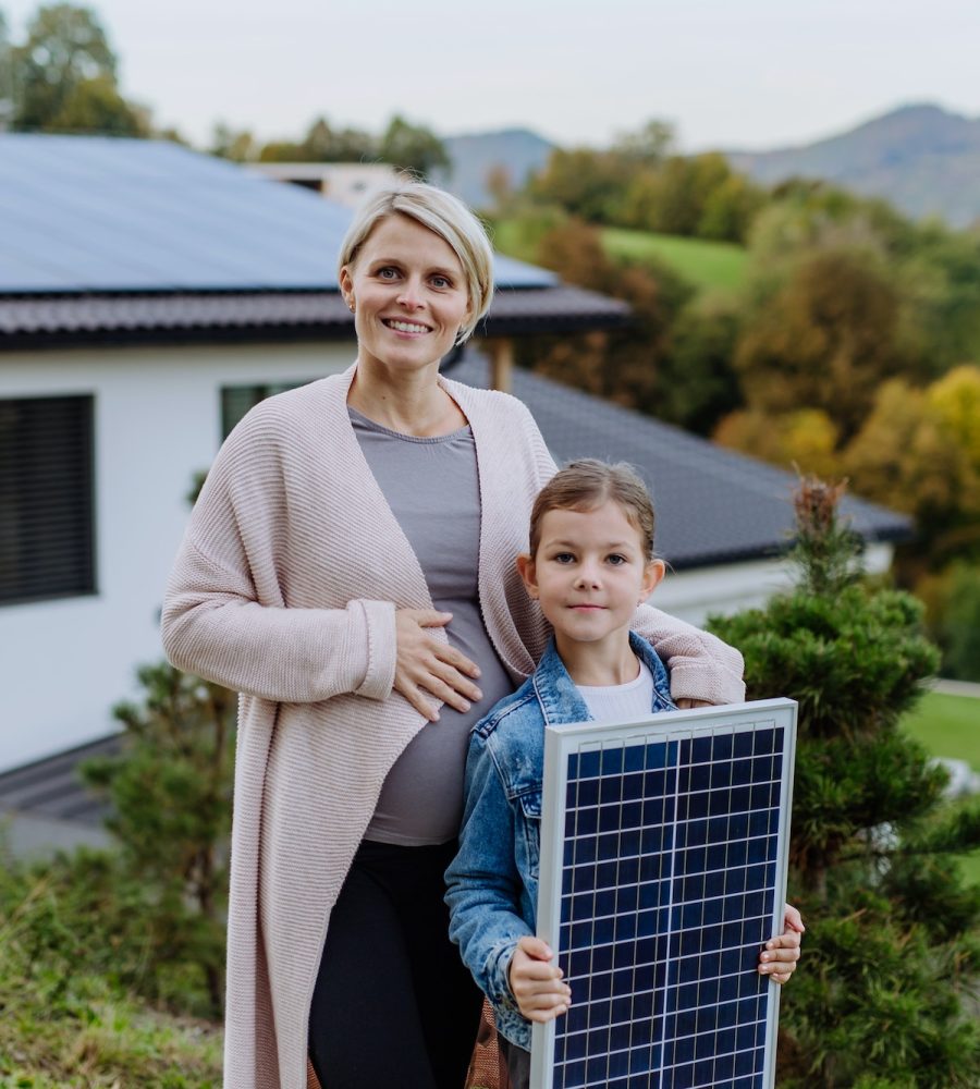 Madre con su pequeña hija cerca de su casa con paneles solares. Energía alternativa, ahorro